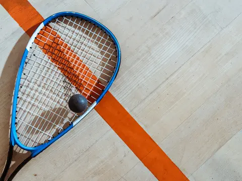 Top view of squash racket and ball on wooden surface Ein Squash-Schläger und ein Squash-Ball liegen auf dem Hallenboden.